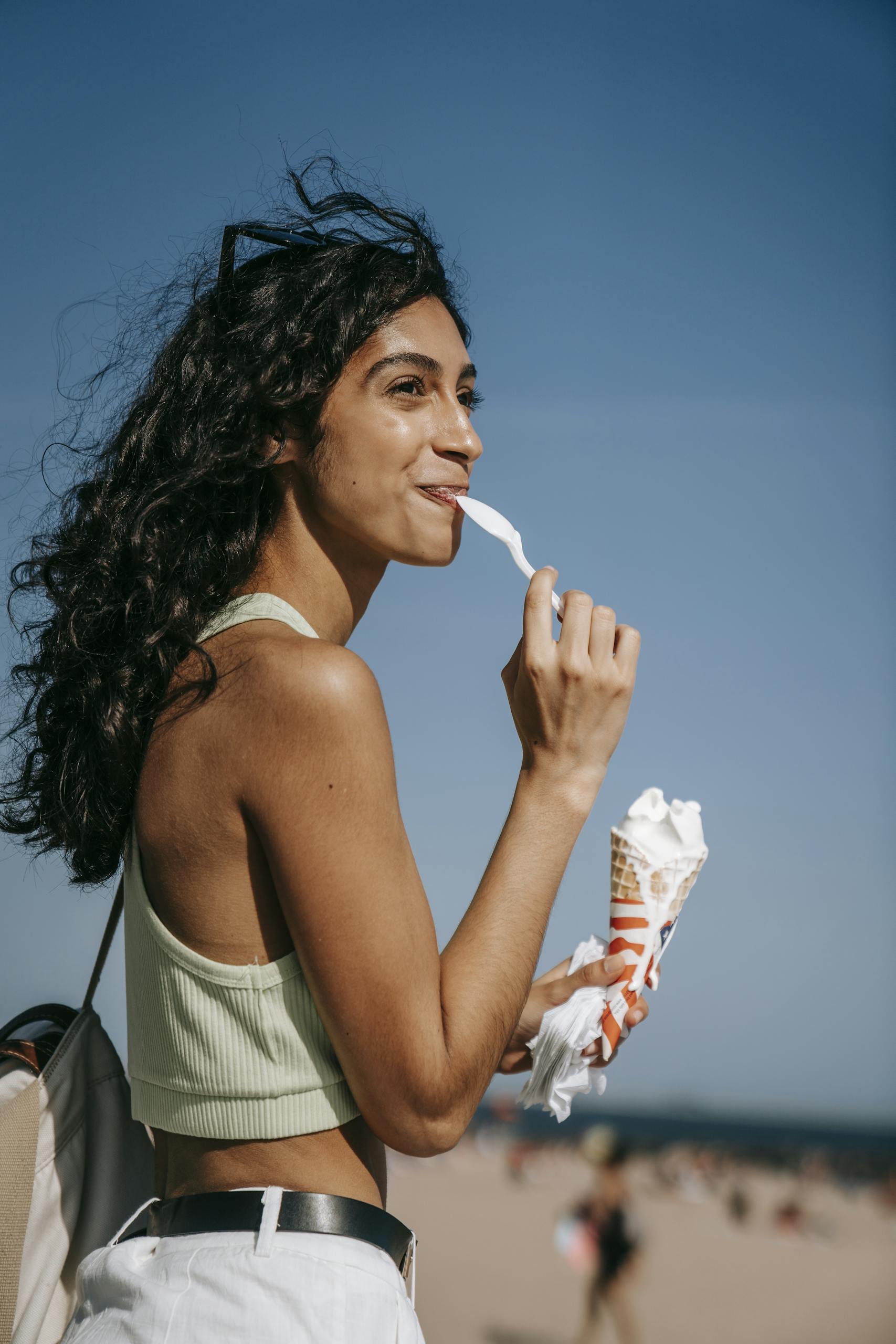 Young woman savoring a vanilla ice cream cone at the beach during summer, embodying leisure and fun.